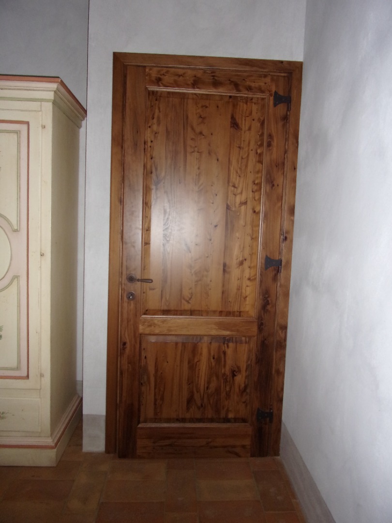 Porta interna in cipresso a un anta con due formelle verniciate color castagno ferrate con alette e T in ferro invecchiato